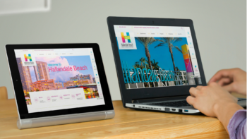 Laptop and tablet on a wooden table displaying the website homepage of Hallandale Beach, FL