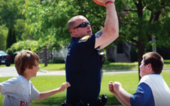 A policeman playing ball with two kids in a park